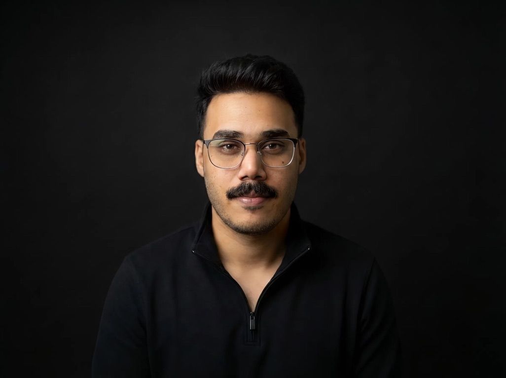 Umair Ali Khan in glasses and a black quarter-zip, against a dark background.