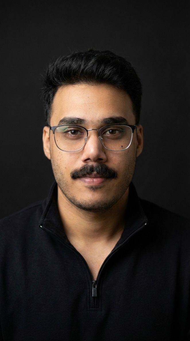 Umair Ali Khan in glasses and a black quarter-zip, against a dark background.